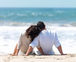 Rear view of a couple sitting on beach with woman leaning head on man's shoulder